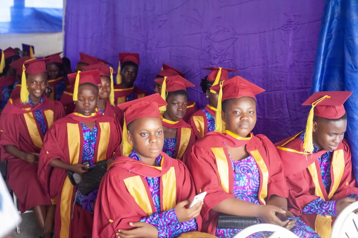 Graduands of Sunset Montessori School seated in maroon and gold gowns at the graduation ceremony