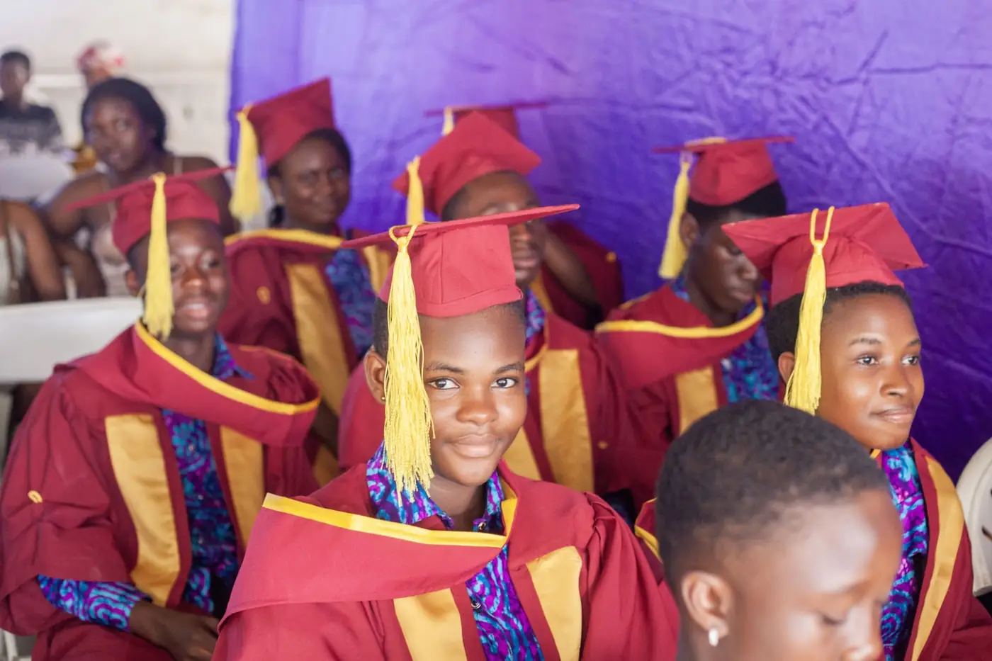 A graduand smiling among classmates in maroon caps and gowns at the graduation ceremony