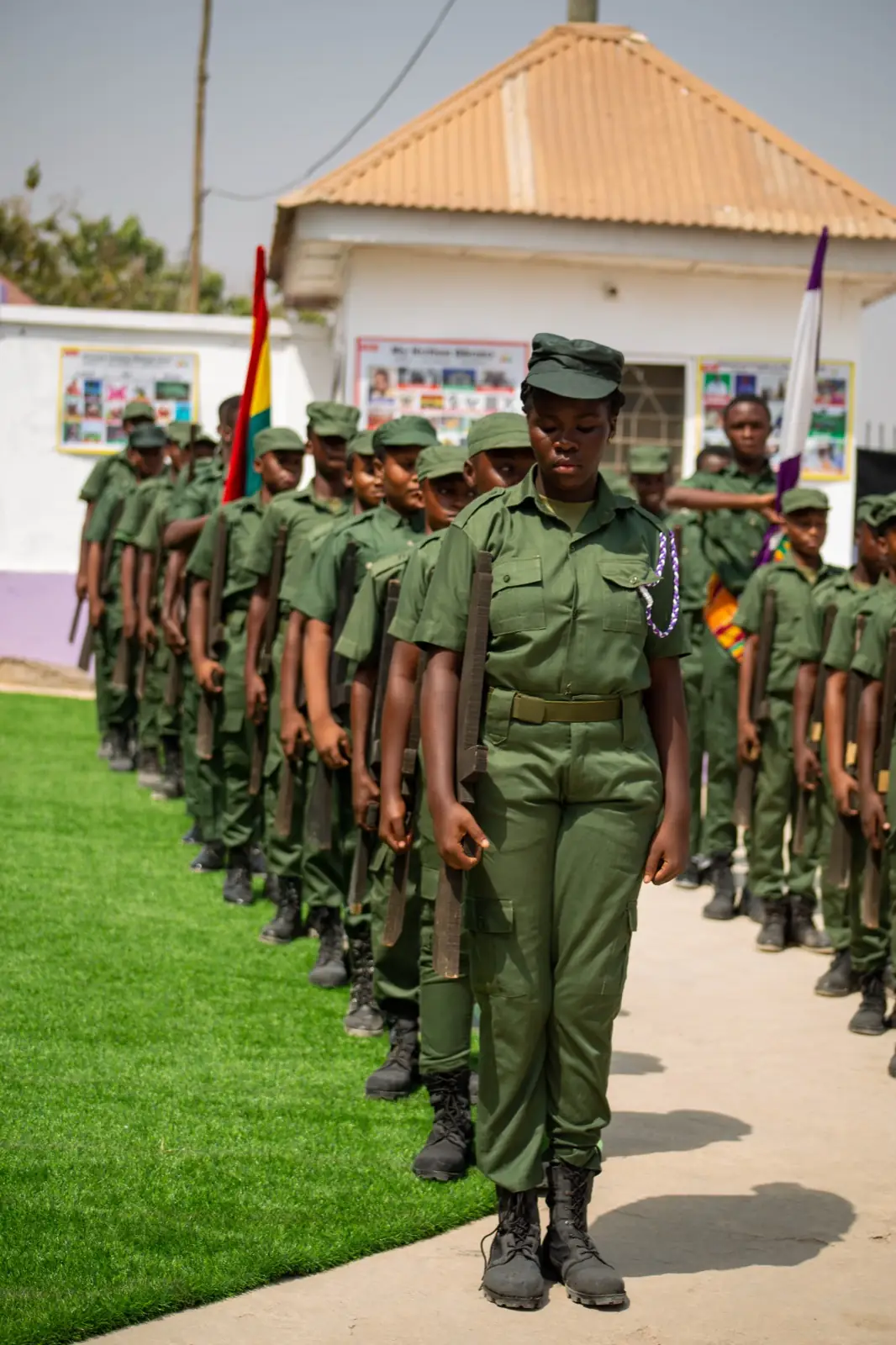 A line of pupils in green parade uniform marching in formation past the school building